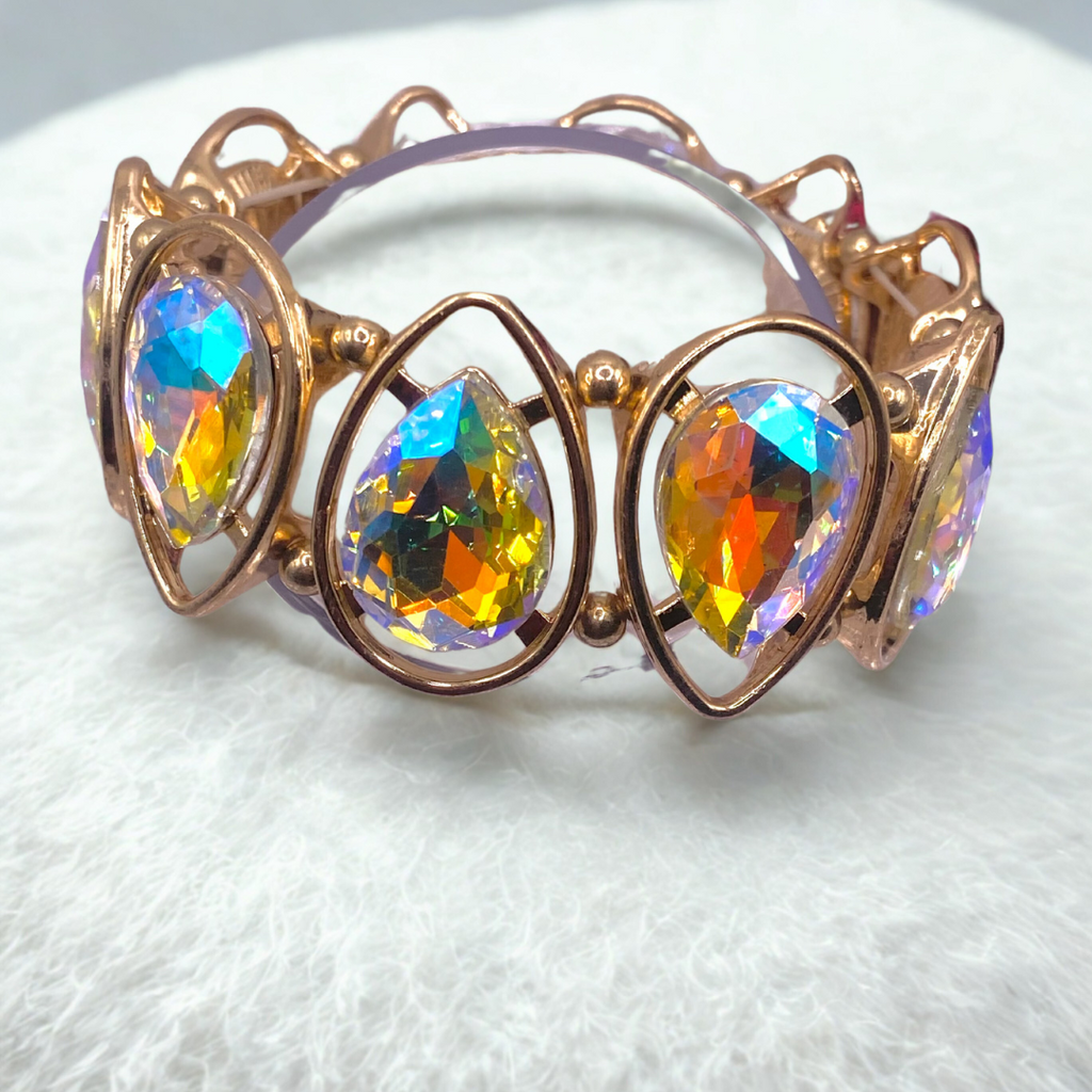 A gold bracelet with multicolored rhinestones, displayed on a white fuzzy surface.
