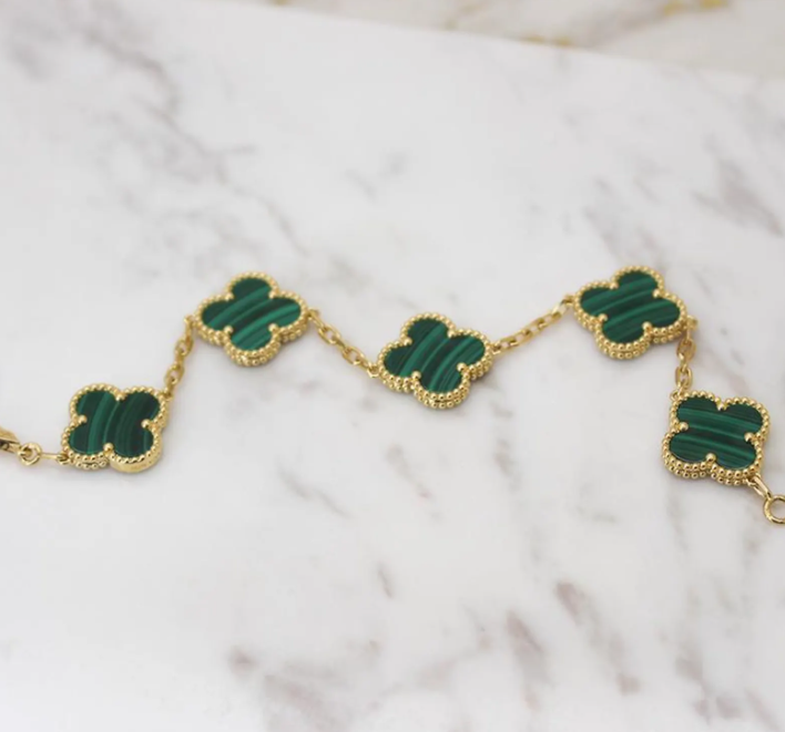 Gold bracelet with green clover-shaped stones on a marble surface